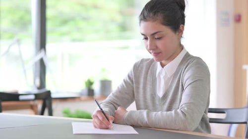 Young Woman Writing on Paper at Desk Indoors