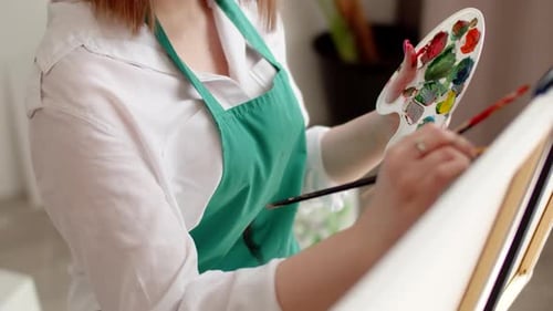 Woman Artist Master Paints on Canvas in Workshop Dips Brush Into Palette with Paints Closeup Top