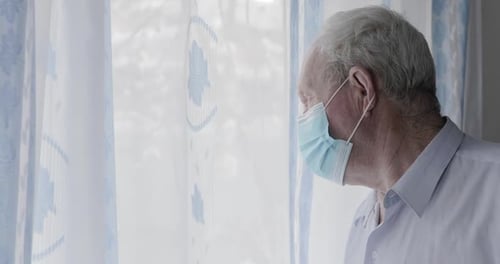 Senior Man in Mask Looks out Window