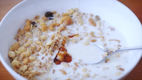 Pouring Honey on Granola with Milk in Bowl