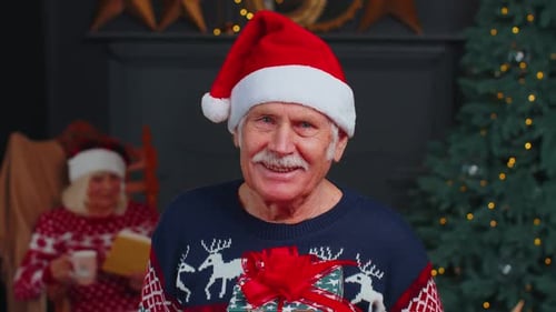 Senior Man Smiles with Gift near Christmas Tree