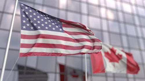 Waving Flags of the USA and Canada in Front of a Skyscraper