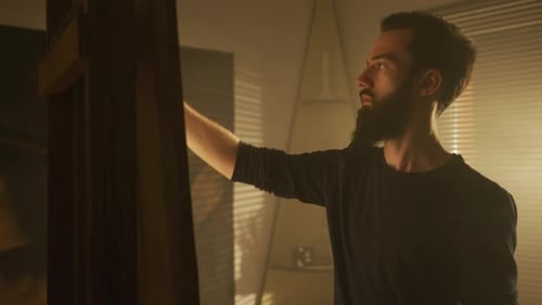 Man Painting on Canvas in Low Lit Room