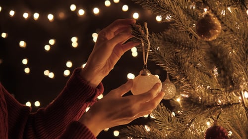 Woman Decorates Christmas Tree with Ornament at Night