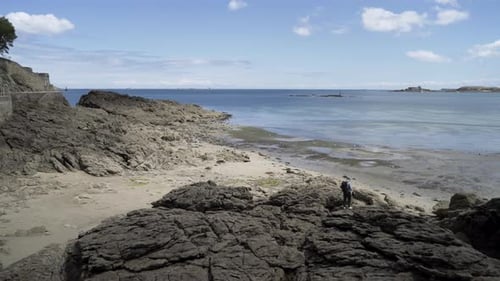 Woman Walks on Rocky Beach Along Blue Ocean Coastline