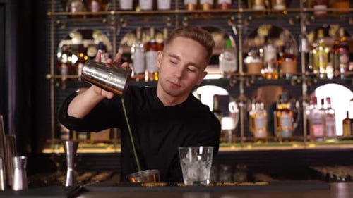 Professional Young Barman Mixing Ingredients of Alcoholic Cocktail By Shaking Shaker Standing on Bar