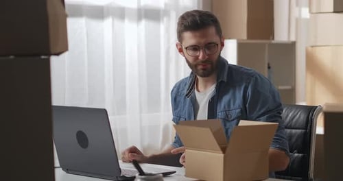Young Male Owner with Laptop Finished Counting Items in Cardboard Box in Warehouse