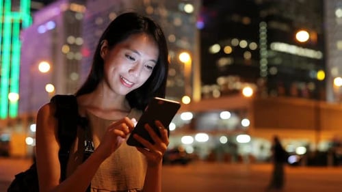 Woman Using Tablet Device in Vibrant City at Night
