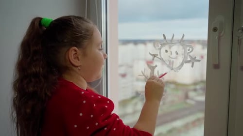 Child draw santa's gnome on window with white paints close-up. Caucasian female person decorate room