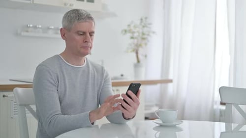Man Uses Smartphone at Bright Kitchen Table