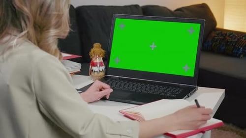 Woman Writing Notes Next to Laptop with Green Screen