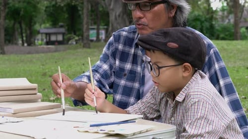 Boy and Senior Man Painting Together in Park