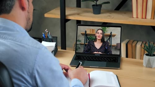 Un étudiant étudie en ligne par conférence vidéo sur ordinateur portable, écrit dans un bloc-notes