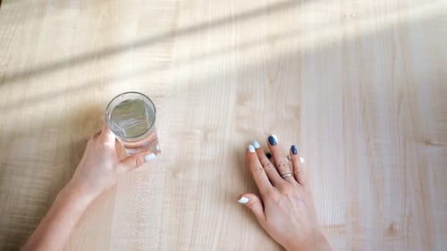 Woman with pills on table next to water