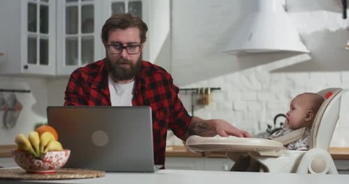 Man Working on Laptop with Baby in Kitchen