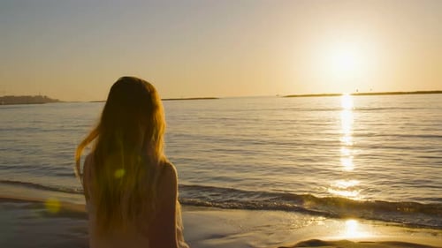 Steadycam shot of a Young attractive woman walking on the beach during sunset