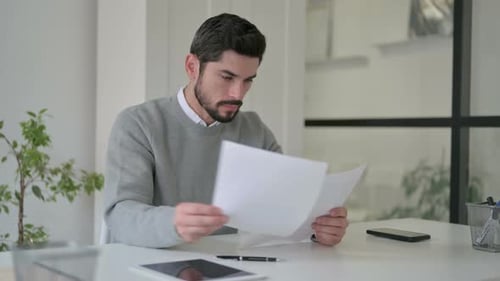 Young Man Upset While Reading Documents in Office