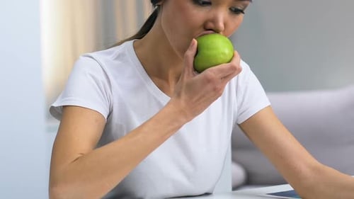 Female Freelancer Looking Through Graphs, Biting Apple and Feeling Pain, Carries