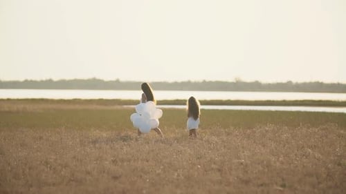 Mother and Child Walking in Grassy Field with Balloons
