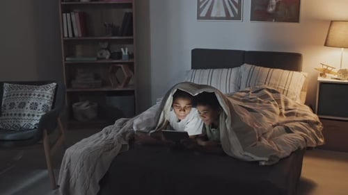 Siblings Using Tablet in Bed