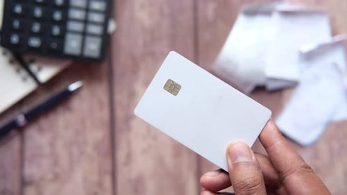 Hand Holding Credit Cards Calculator and Paper on Table