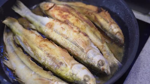 Smelt Fish Is Fried in Oil in a Black Pan. Close-up Shot. Seafood Cooking