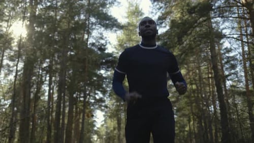 Young Fit Afroamerikaner beim Joggen auf einer Waldstraße.