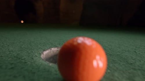 An orange mini golf ball falls into the golf hole and bounces in the pocket on a course.