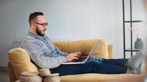 Man Relaxing on Sofa Typing on Laptop