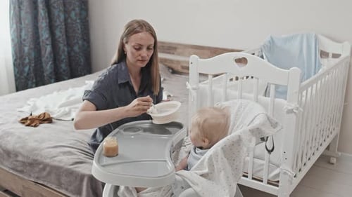 Woman feeding baby in high chair at home