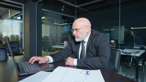 Middle Aged Caucasian Male Confident Bearded CEO Sitting at Table Surfing Internet on Laptop