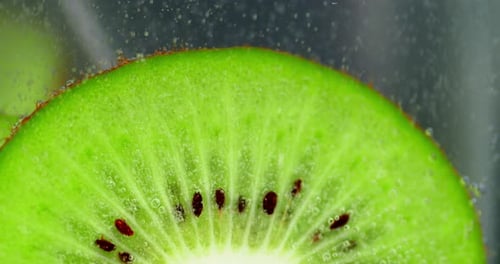 Un trozo de kiwi verde bajo el agua con burbujas de aire.