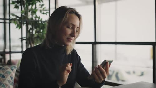 Attractive Blonde Woman Uses a Smartphone in a Cafe