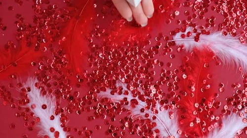 Hand Placing Gift Box on Red Sequins and Feathers