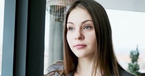 Porträt einer jungen attraktiven Frau, die im Büro neben dem Fenster in die Kamera schaut. Fröhlich