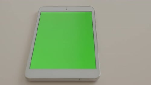 Tablet PC with green screen display tilting on white surface 4K 2160p UltraHD footage - Slow tilt o