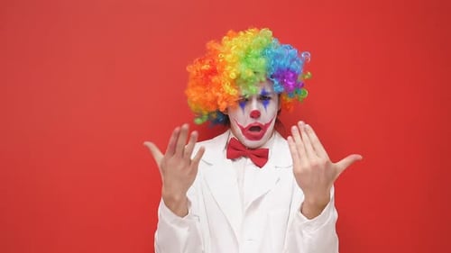 Clown with Rainbow Wig Gesturing Against Red Background