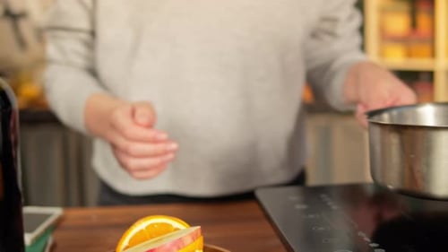 Woman Cooking Mulled Wine Gluhwein with Apples and Oranges Recipe