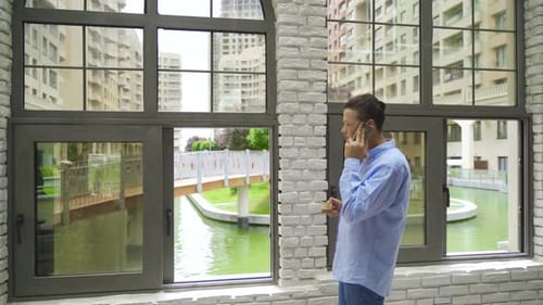 Young Adult Talking on Phone by City Window