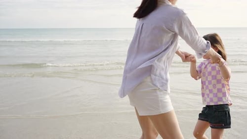 4K asiatische Mutter hält Hand und spielt mit kleiner Tochter am Strand bei Sonnenuntergang im Sommer.