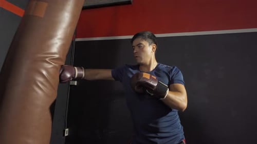 Strong caucasian man punching bag, combat punches in boxing sport club workout at training