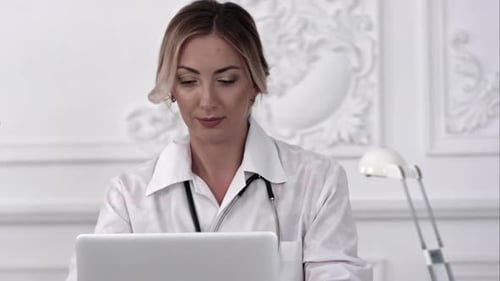 Female Doctor Sitting on the Desk and Working a Laptop in Hospital