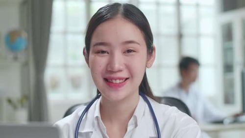 Close Up Young Asian Woman Doctor Is Using Laptop Computer And Smiles To Camera In Workplace