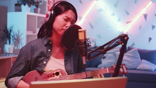 Asian Woman Singing and Playing the Guitar in Home Recording Studio
