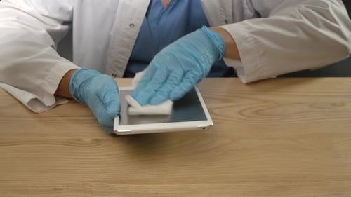 Adult Sanitizes White Tablet with Gloves and Wipe