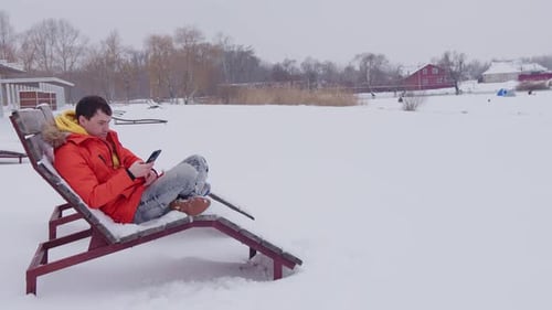 Man Uses Mobile Device While Relaxing in Snow