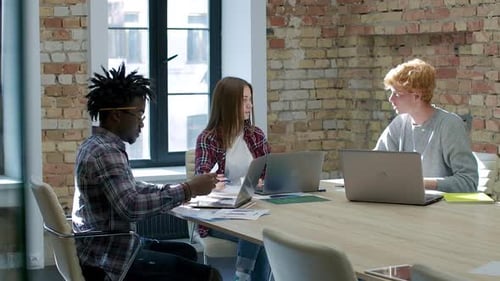 Wide Shot of Young Caucasian and African American Colleagues Sitting with Laptops in Office and