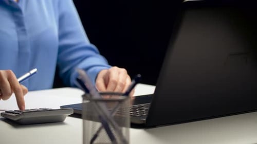 Frau mit Taschenrechner und Laptop im Nachtbüro