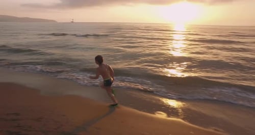 Criança correndo na praia durante o pôr do sol