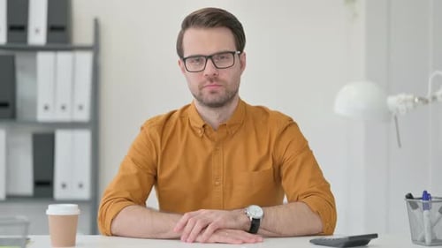 Man Sits at Desk Looking at Camera